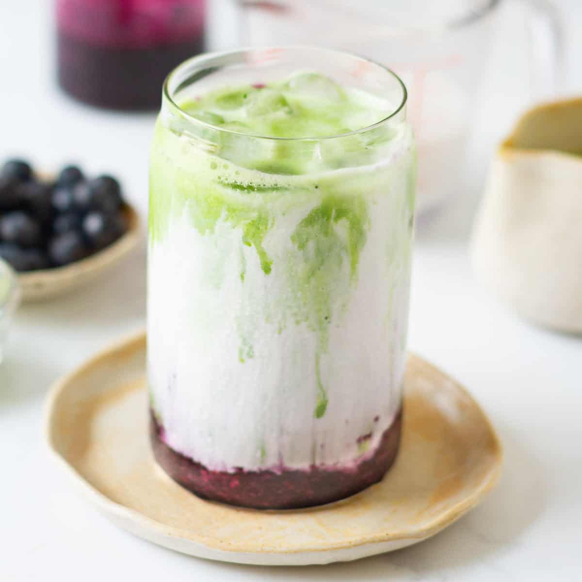 Blueberry matcha latte in a glass on a small plate.