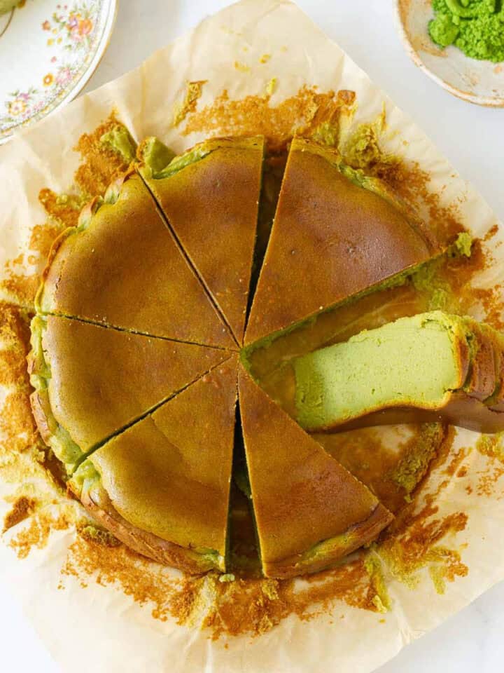 Matcha cheesecake cut into 8 slices with one slice kept sideways on parchment paper.