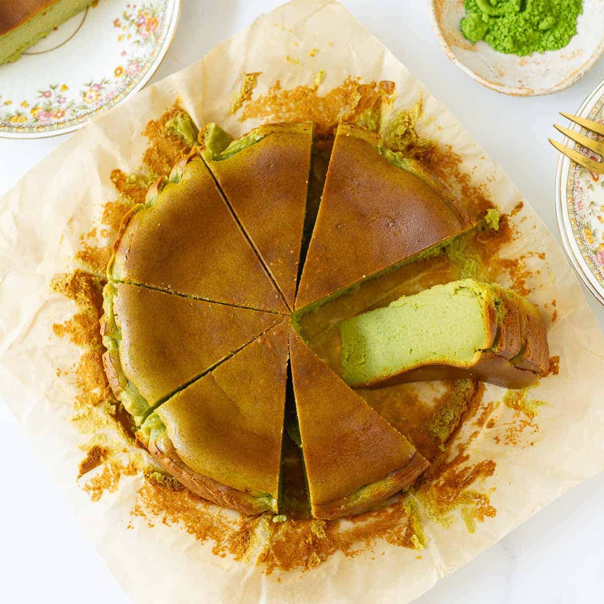 Matcha cheesecake cut into 8 slices with one slice kept sideways on parchment paper.