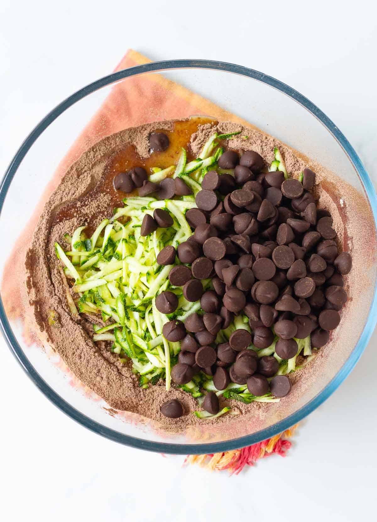 Shredded zucchini and chocolate chips on top of cake ingredients in a bowl.