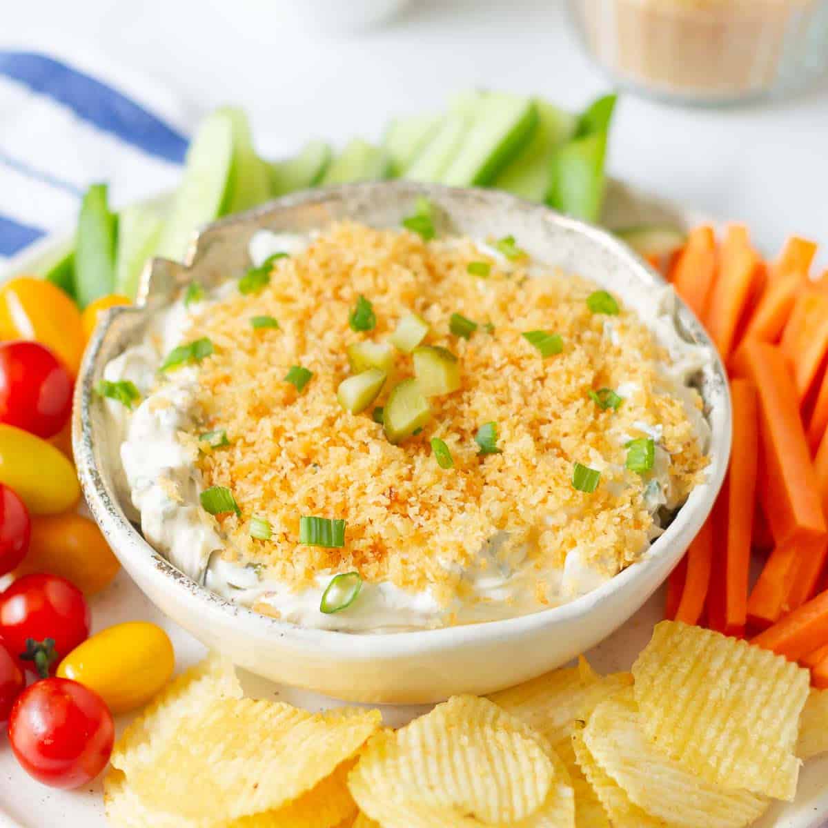 Pickle dip with toasted panko breadcrumbs on top with veggies and chips around.