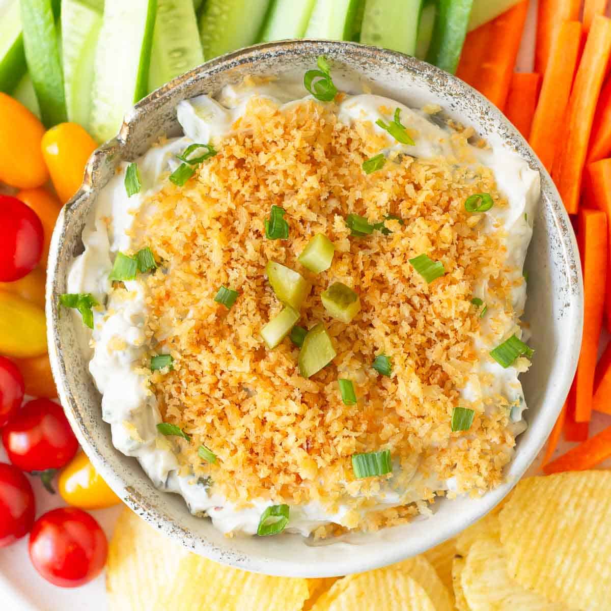 Fried pickle dip in a serving bowl with veggies and chips around.