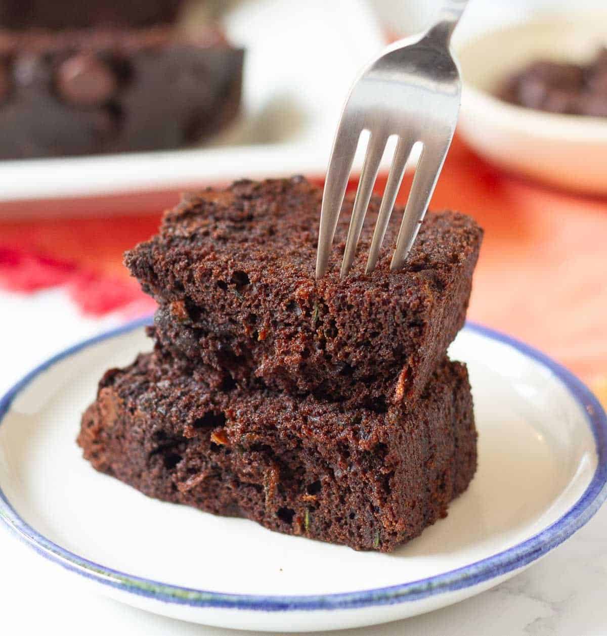 2 halves of a cake slice stacked on a plate with fork on top.