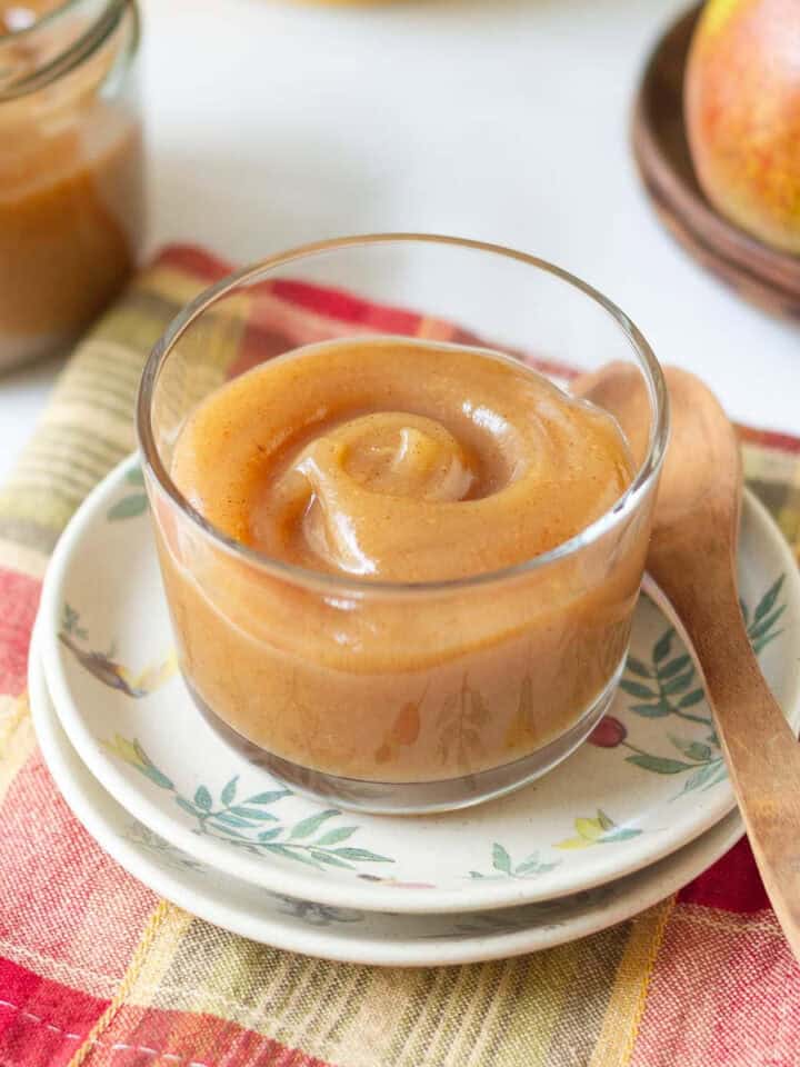 Pear butter in a glass container with a wooden spoon on the side.