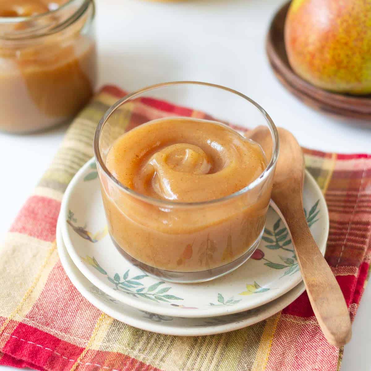 Pear butter in a glass container with a wooden spoon on the side.
