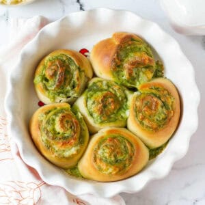 Cheesy pesto swirl rolls in a round baking dish.