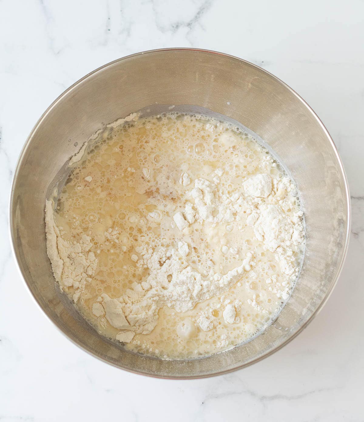 Yeast mixture on top of flour in a mixing bowl.