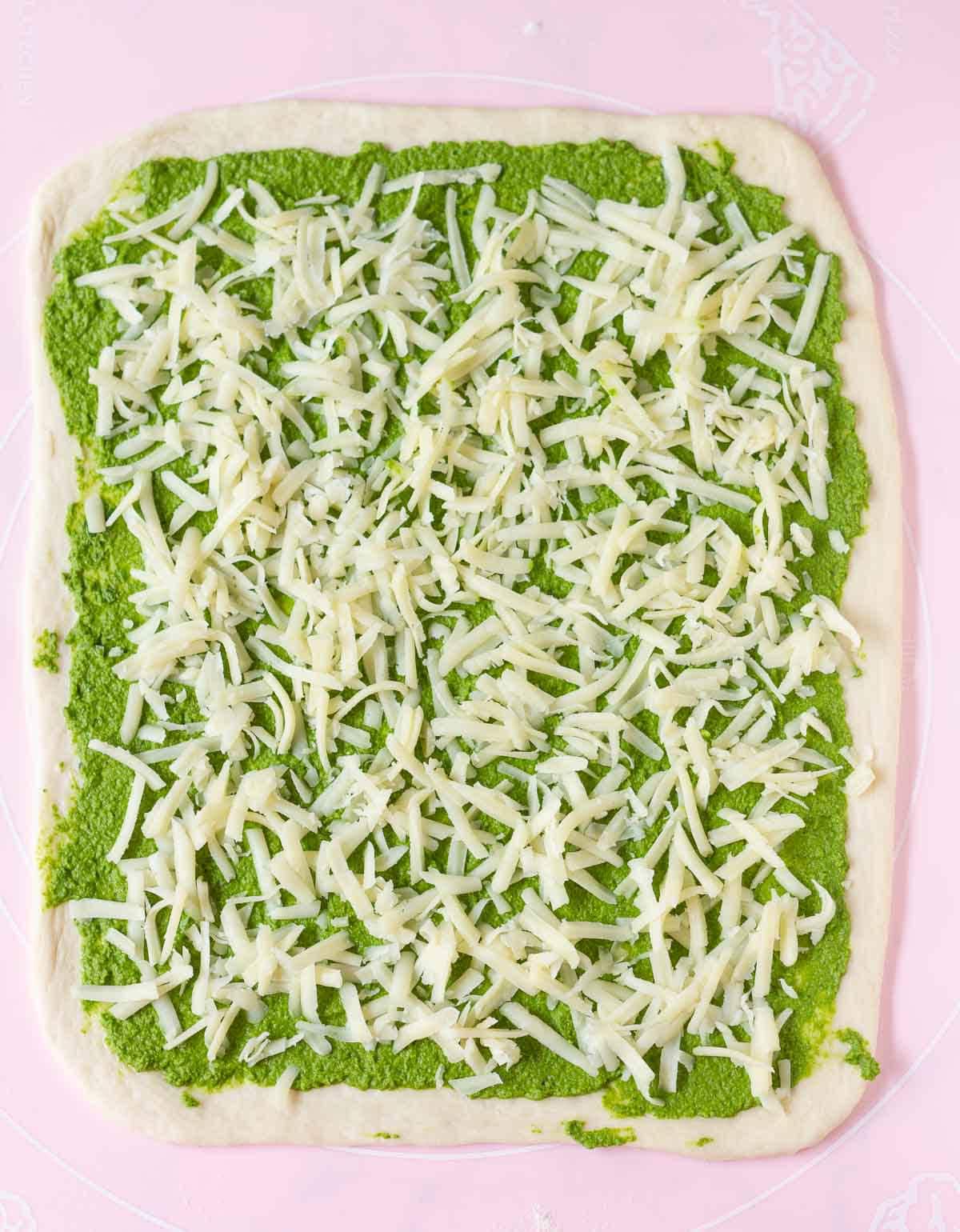 Shredded cheese on top of pesto on rolled out dough.