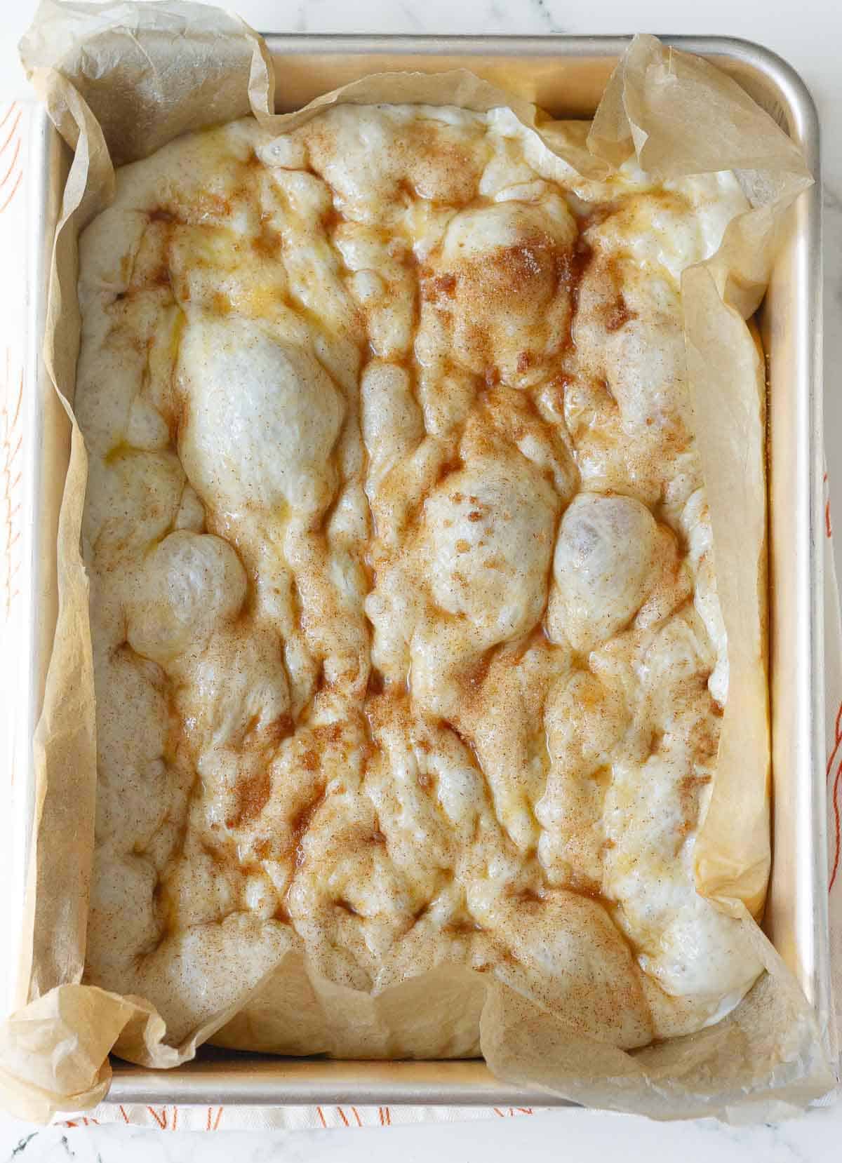 Dimpled focaccia dough on parchment paper.