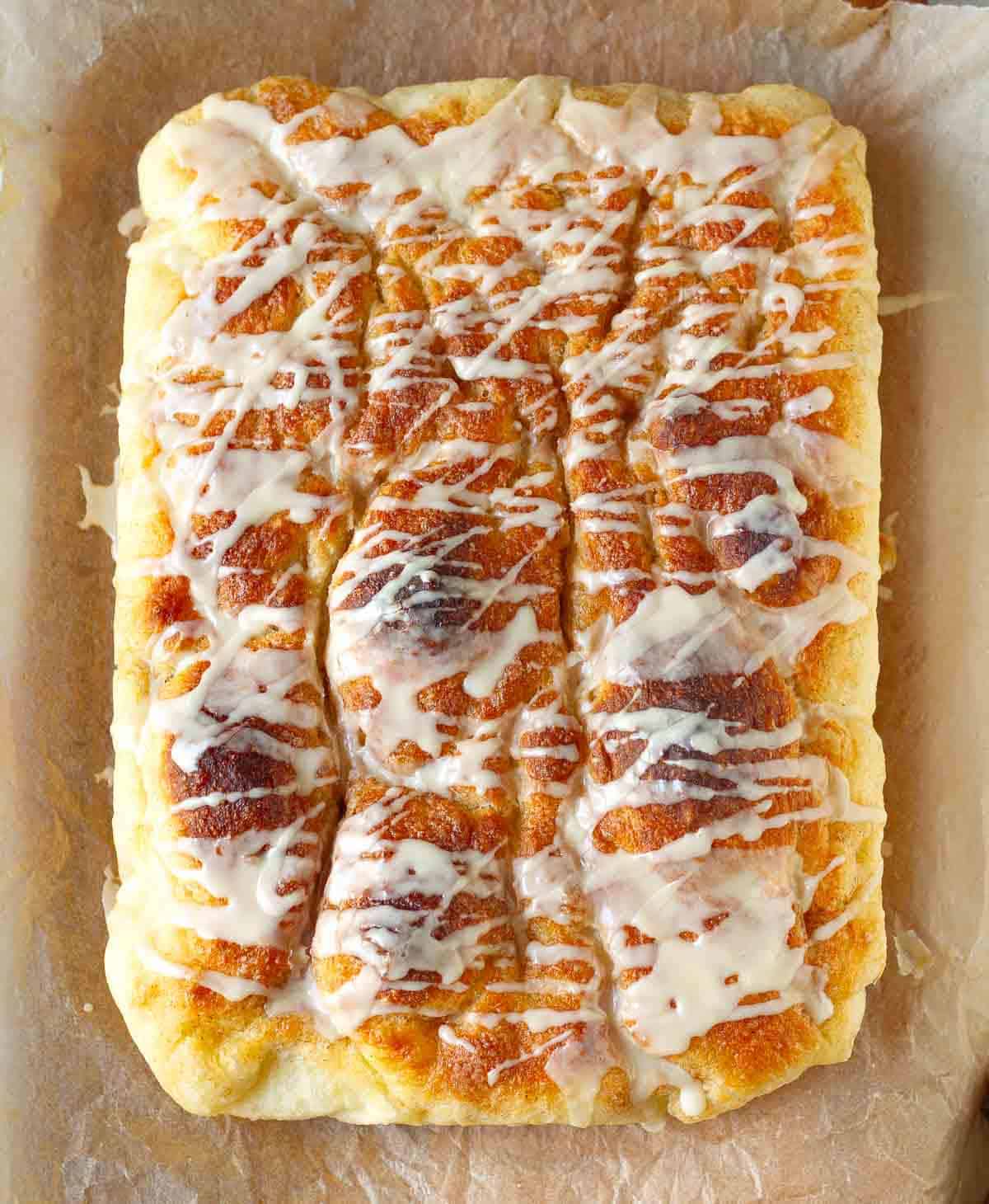Cinnamon focaccia with vanilla icing on parchment paper.
