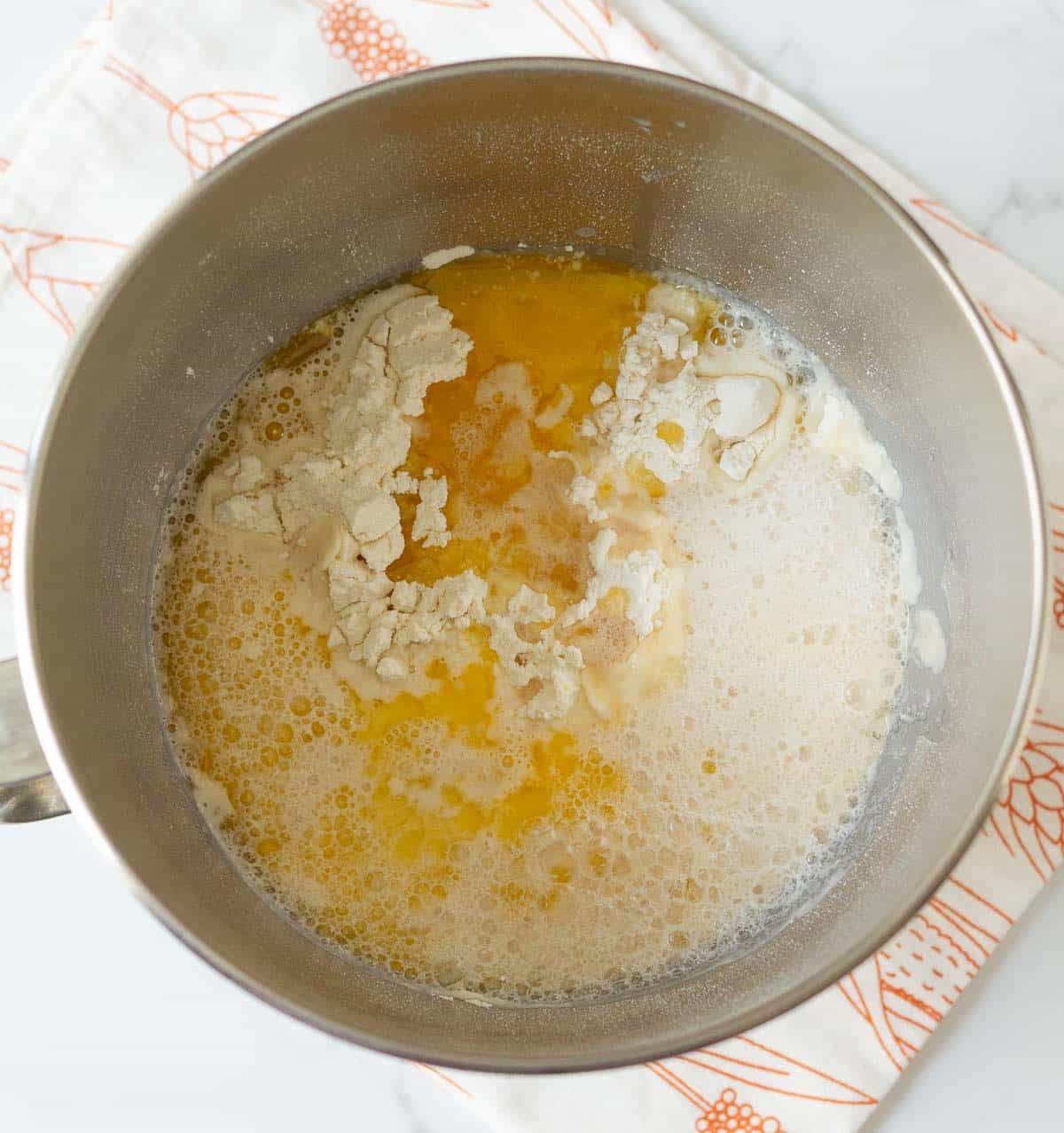 Flour, melted butter, and yeast mixture in a stand mixer's bowl.