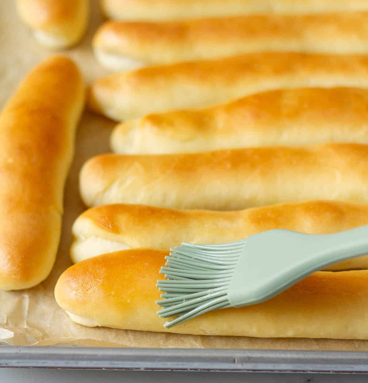 Brushing melted butter on breadsticks with a pastry brush.