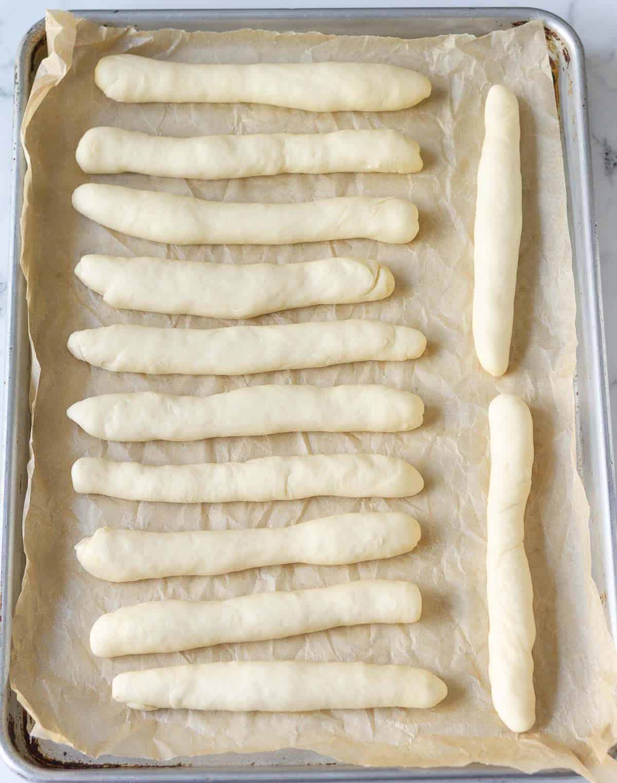 Bread dough shaped into 12 logs on a baking tray.