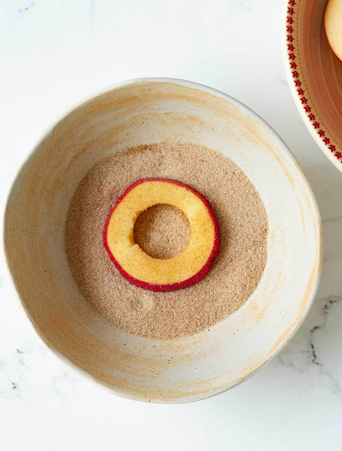 Apple slice in a bowl of cinnamon sugar.