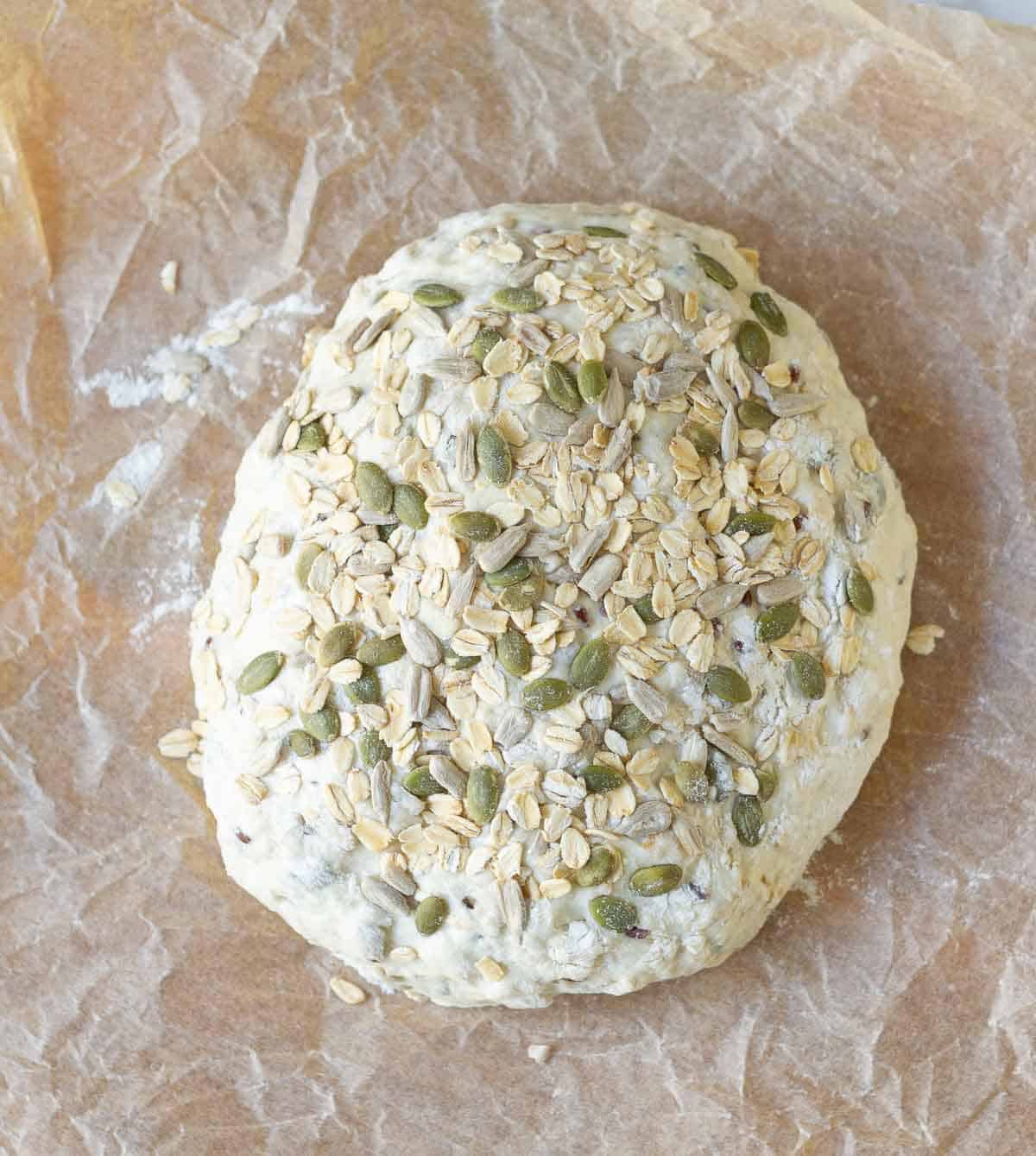 Dough with oats and seeds on parchment paper.