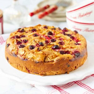 Apple cranberry cake on a white plate with plates and cups in the background.