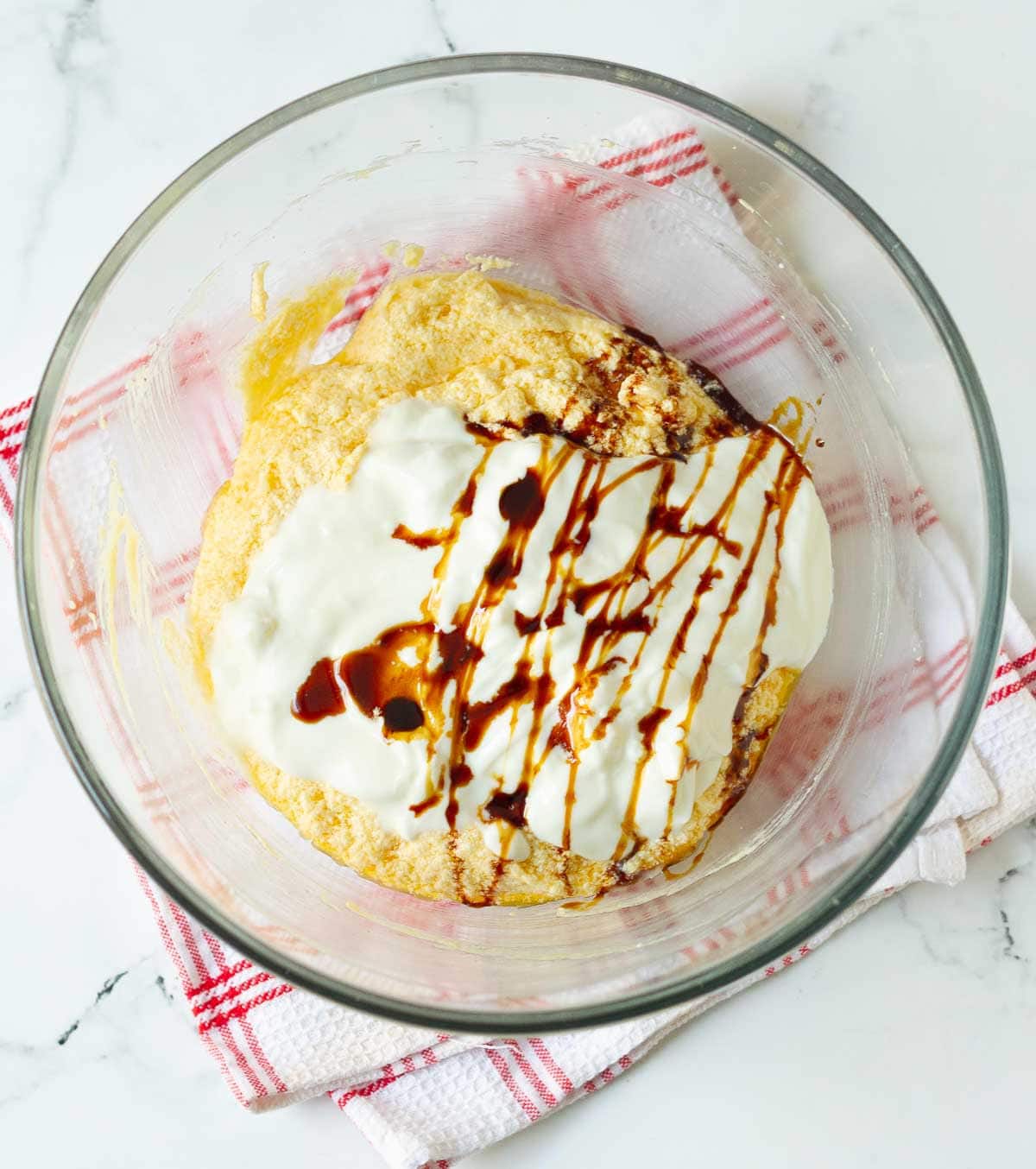 Yogurt and vanilla extract on butter-sugar mixture in a mixing bowl.
