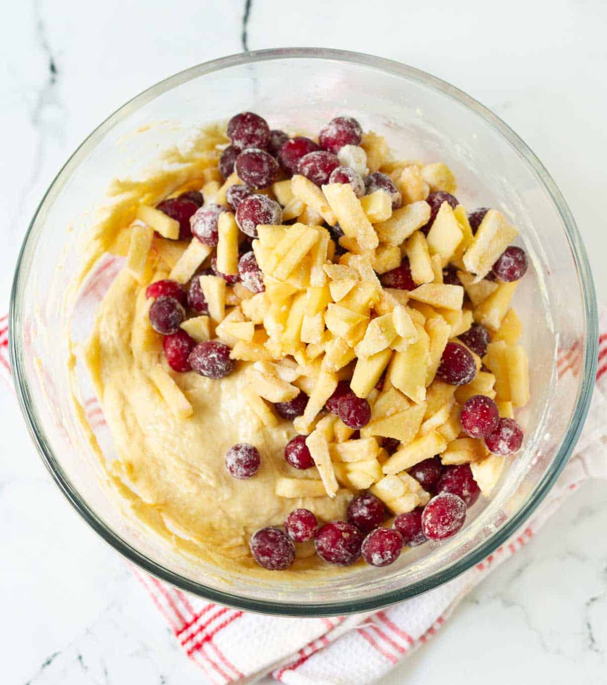 Apples and cranberries on top of cake batter in a bowl.