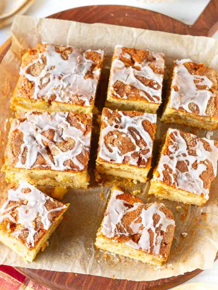 Apple fritter cake cut into 9 pieces on parchment paper.