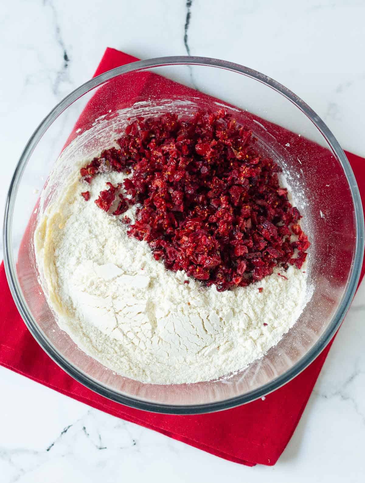 Cranberries and flour on top of butter-sugar mixture in a mixing bowl.
