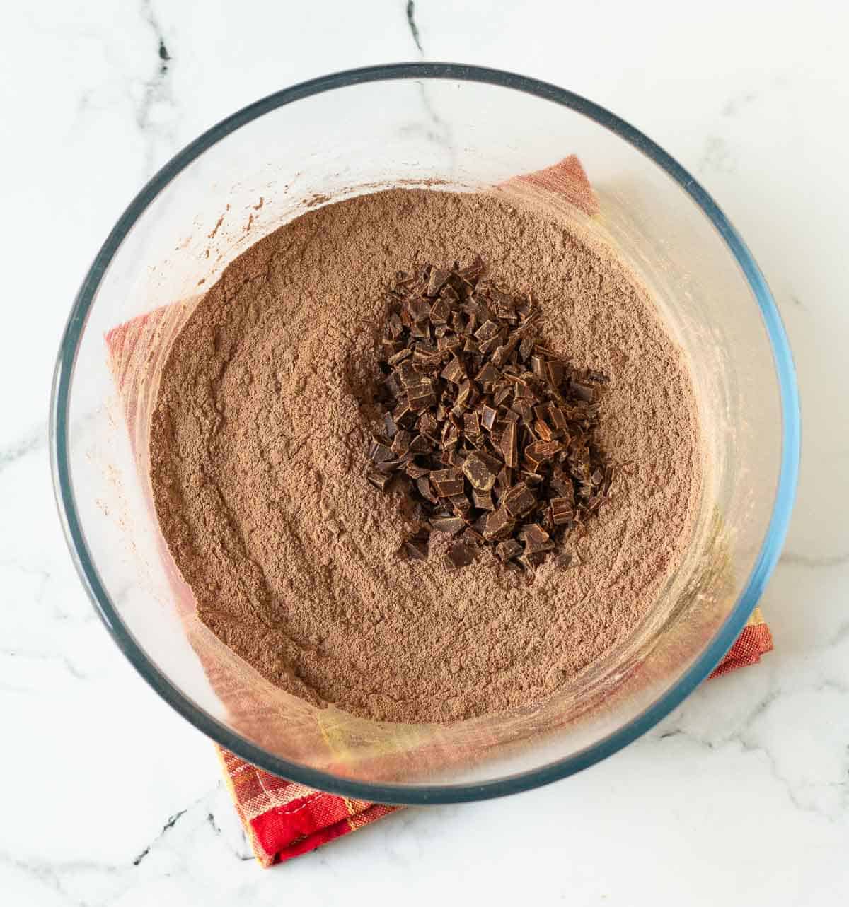 Chopped chocolate on top of cocoa mix in a mixing bowl.