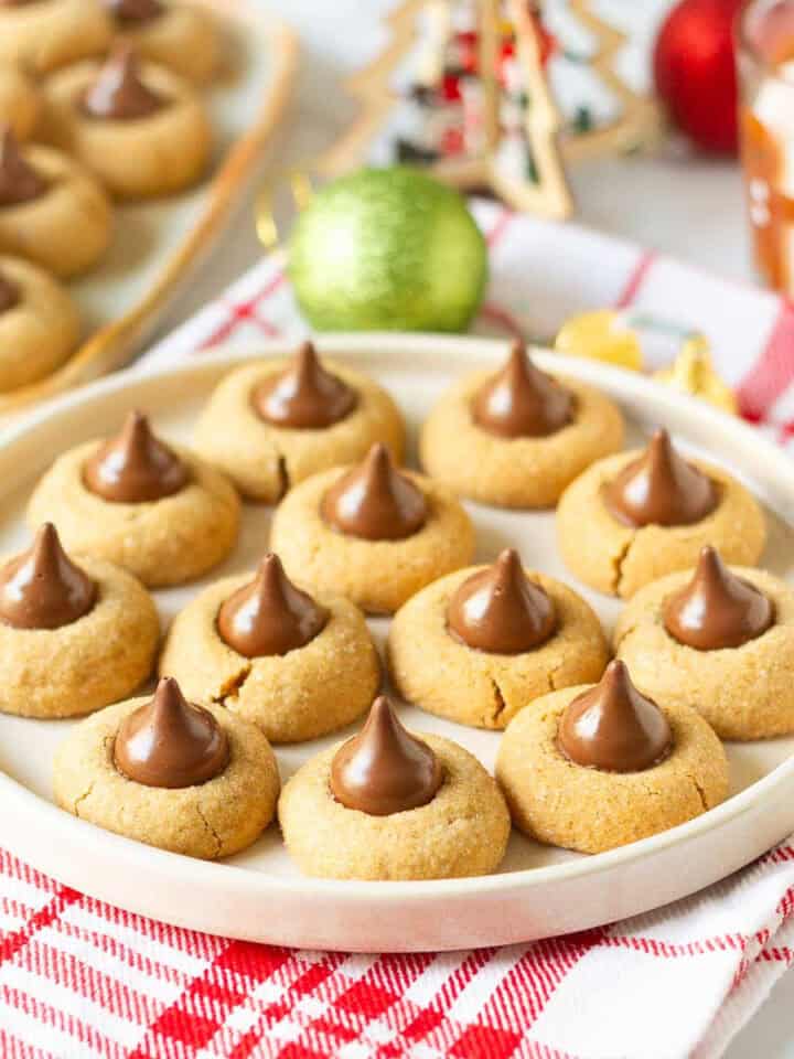 Gingerbread kiss cookies on a round serving platter with more cookies and Christmas decor in the background.