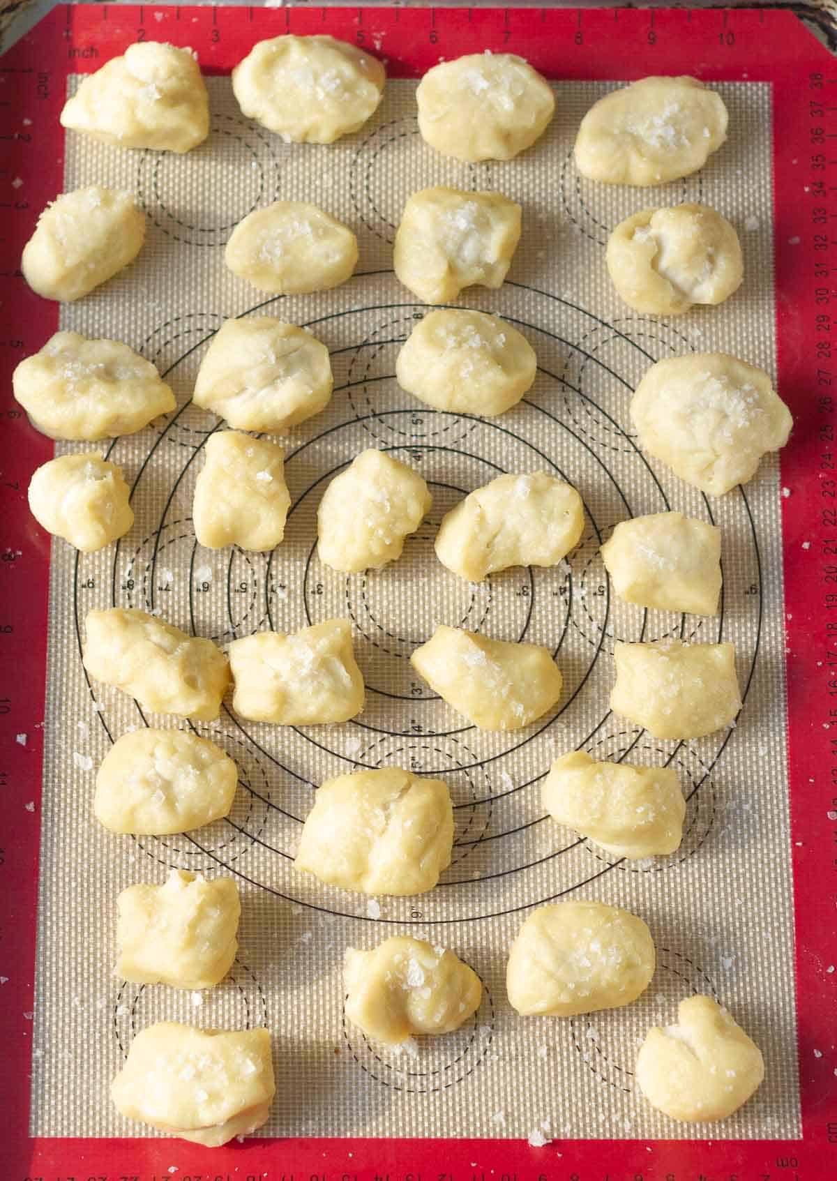 Dough pieces topped with sea salt on a silpat-lined baking tray.