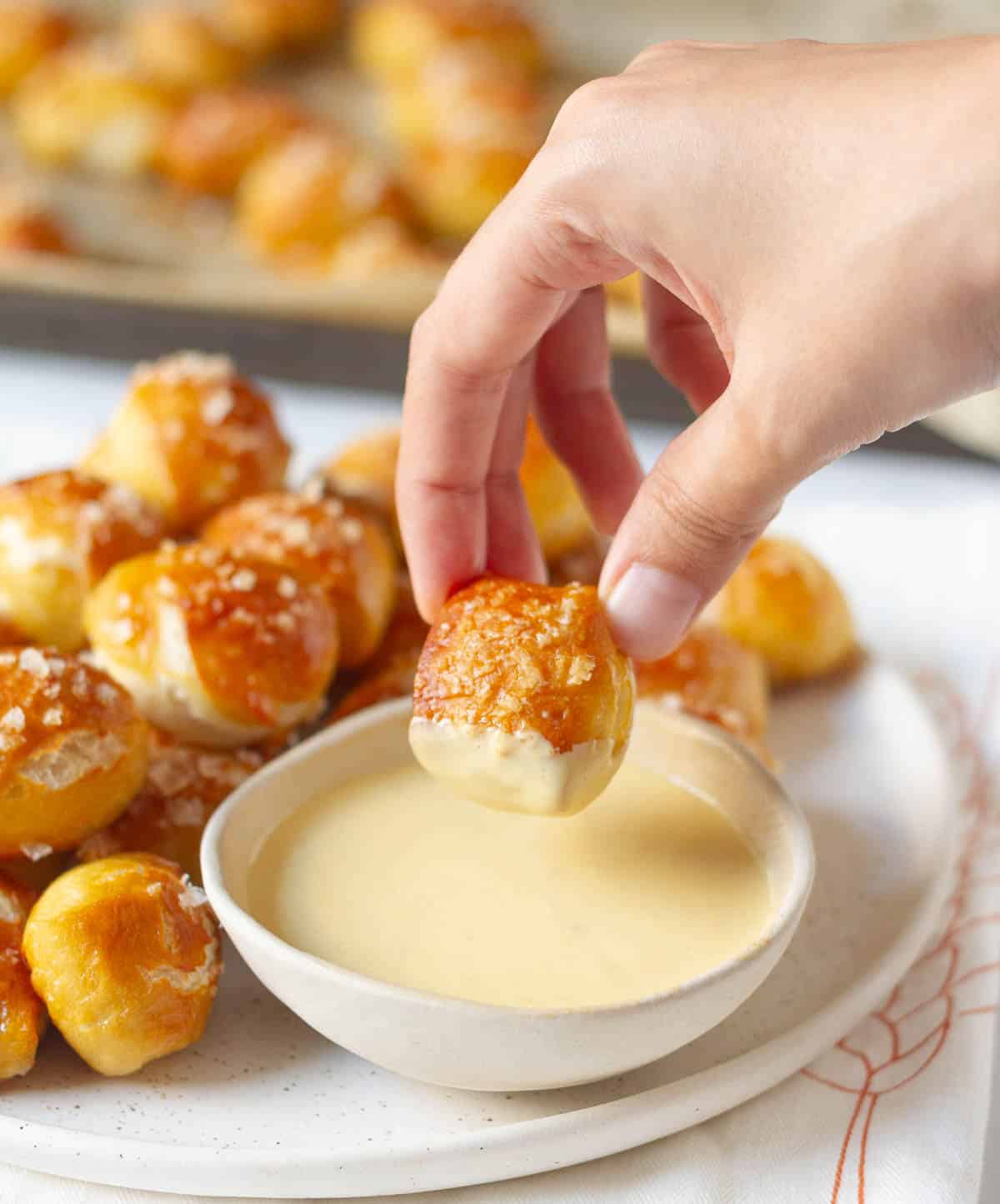 A hand holding a pretzel bite half dipped in a sauce.