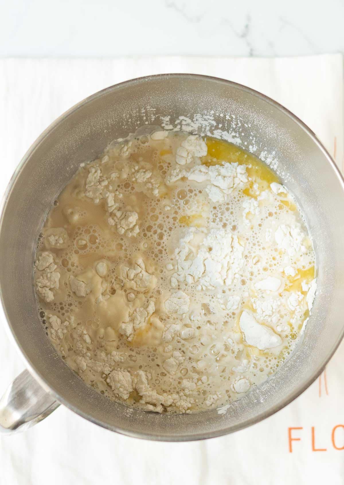 A stand mixer bowl with flour, butter, salt, and yeast mixture.