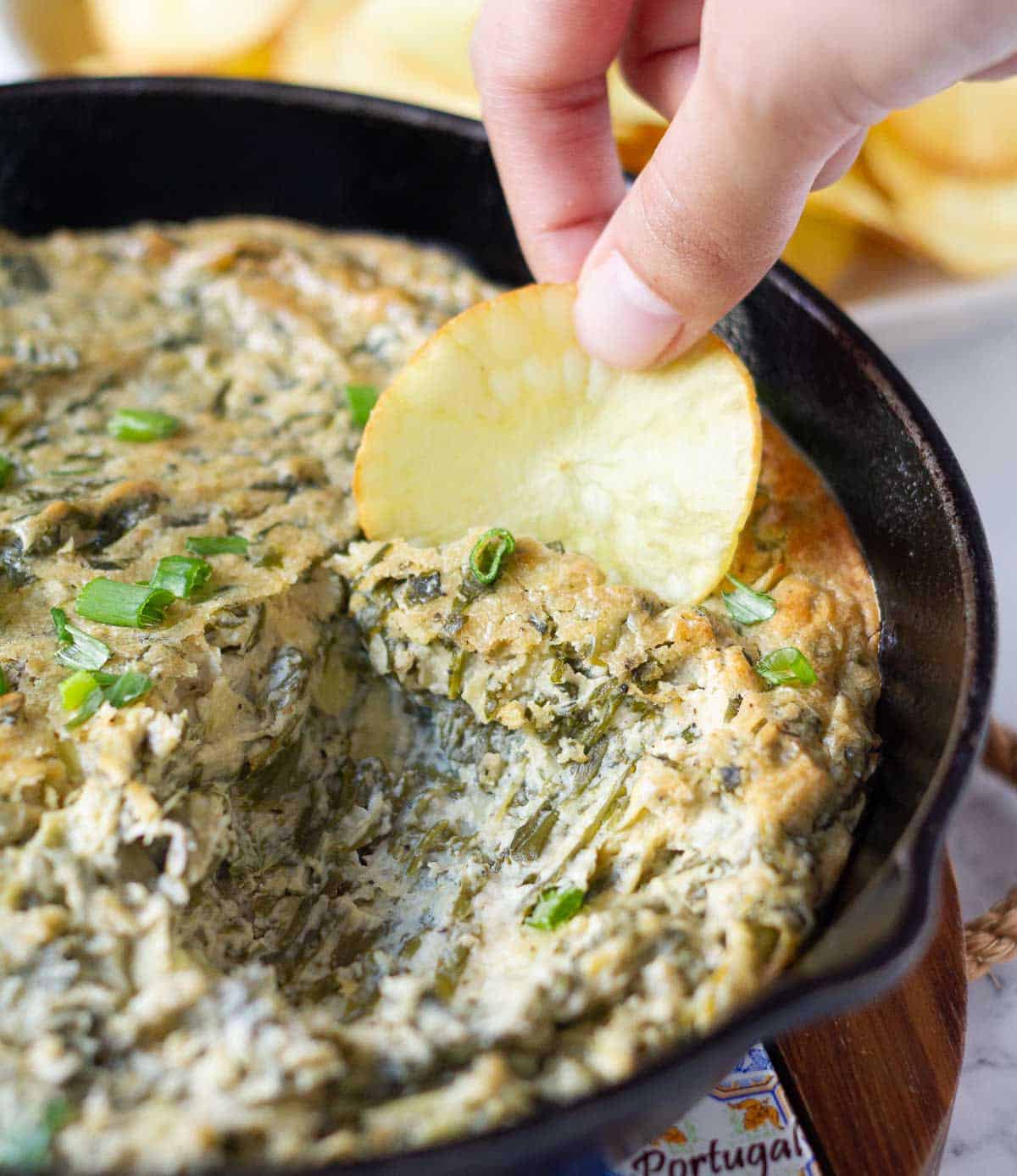 A hand holding a potato chip scooping out some dip.