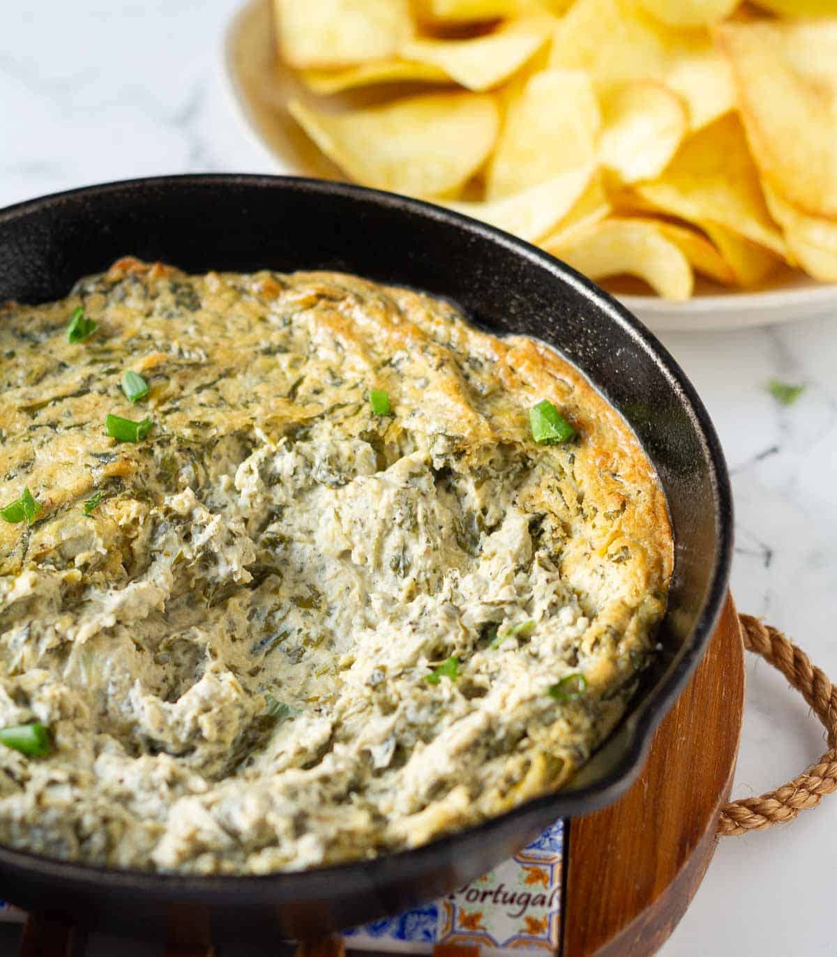 A creamy dip in a black pan with chips in the background.