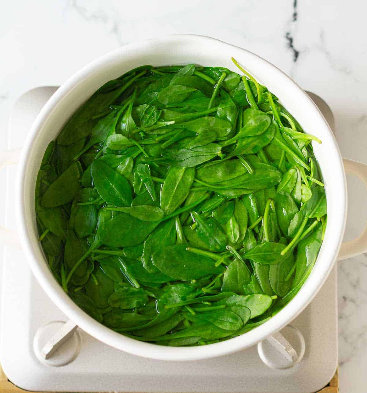Blanching spinach in a pot of boiling hot water.