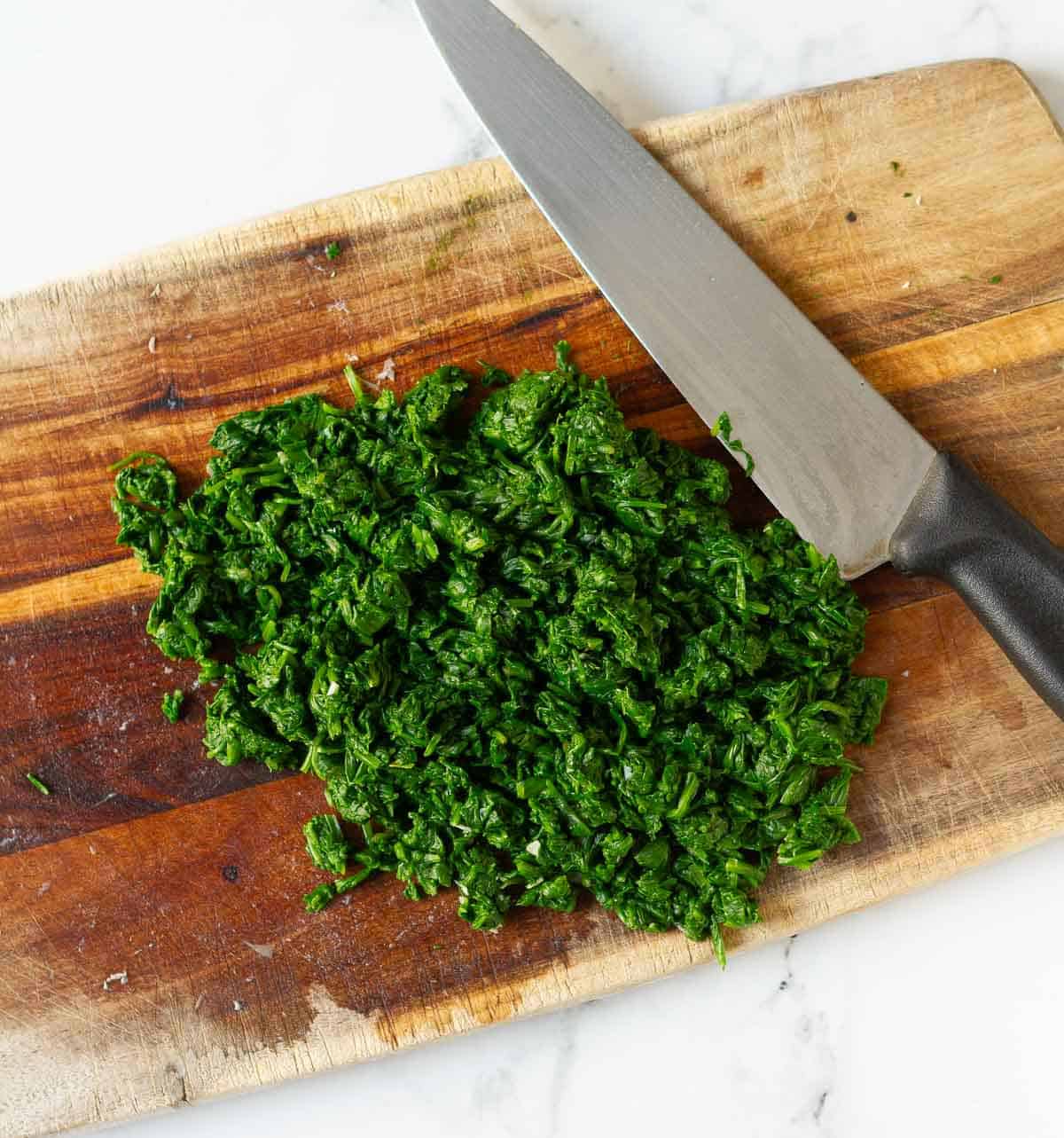 Chopped spinach on a wooden board with a knife.