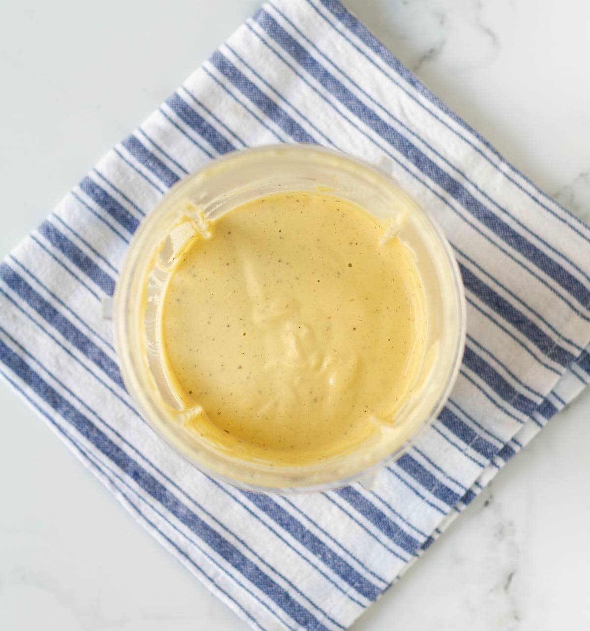 Creamy sauce in a blender jar on a blue striped towel.