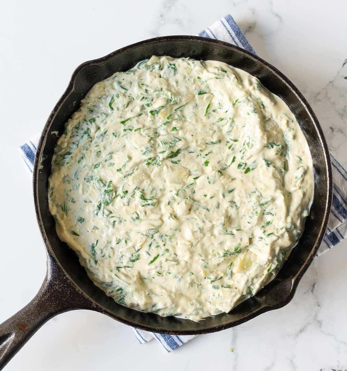 creamy spinach artichoke mixture in a cast-iron pan.