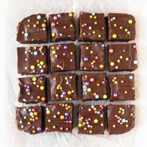 Squares of brownies with frosting and sprinkles on a parchment paper.