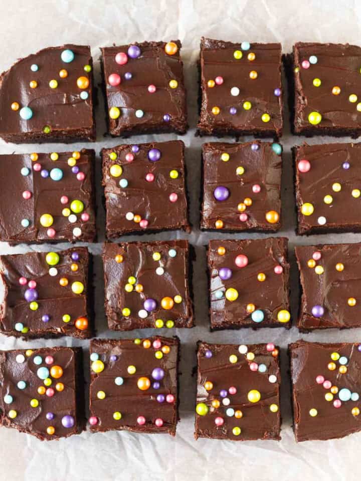 Squares of brownies with frosting and sprinkles on a parchment paper.