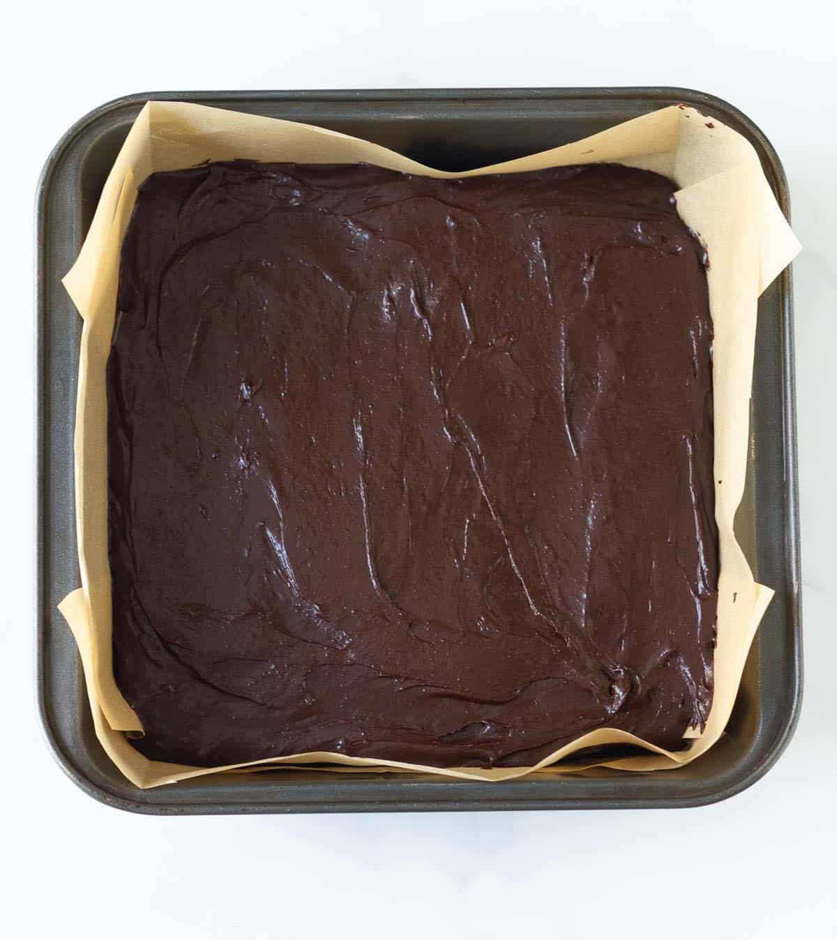 Brownie batter in a parchment-lined square baking pan.