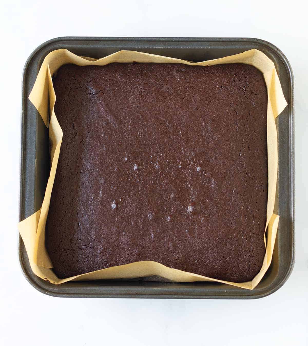 Baked brownie in a parchment-lined square pan.