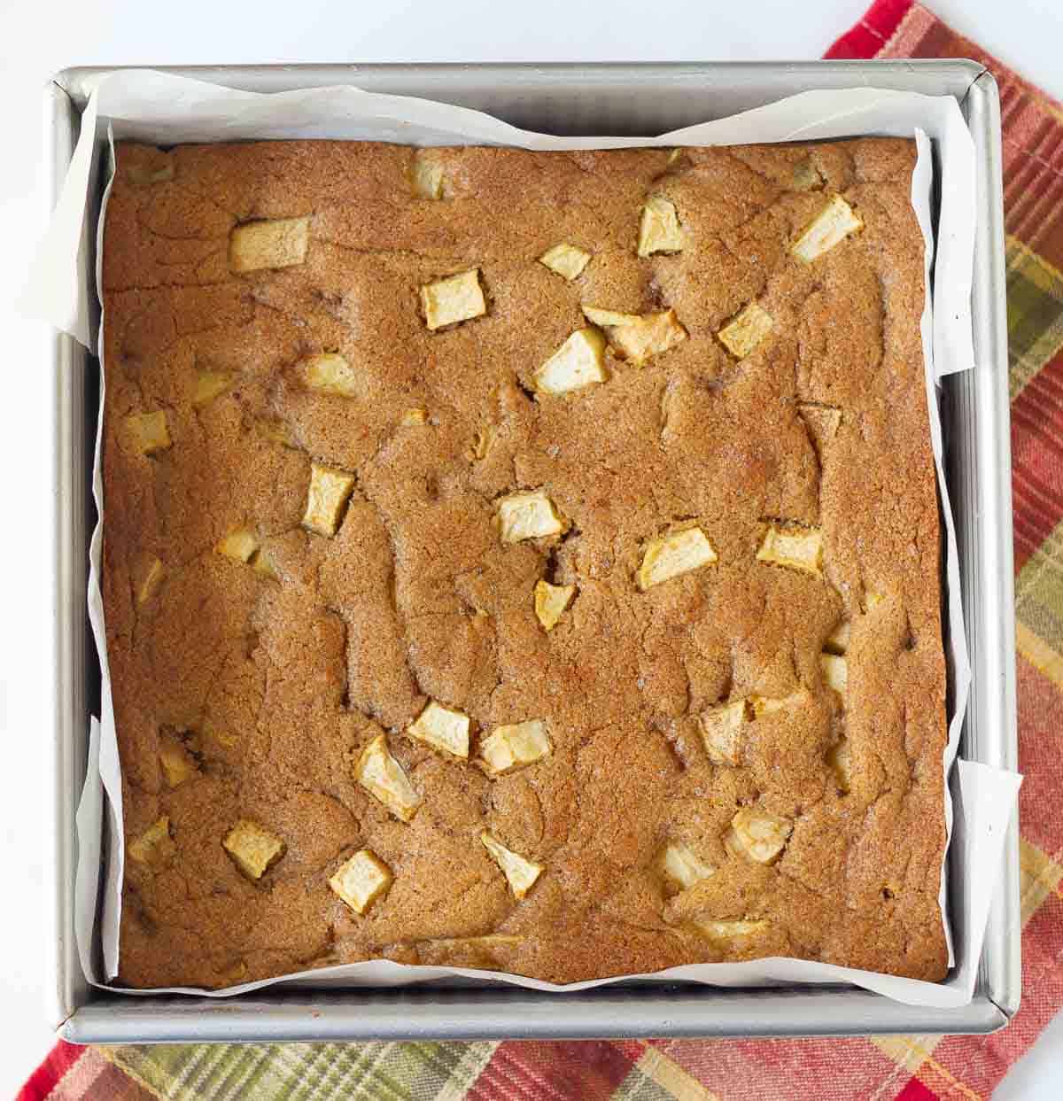 Baked apple blondies in a square pan lined with parchment paper.