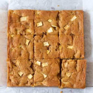 Apple blondies cut into 9 squares on parchment paper.
