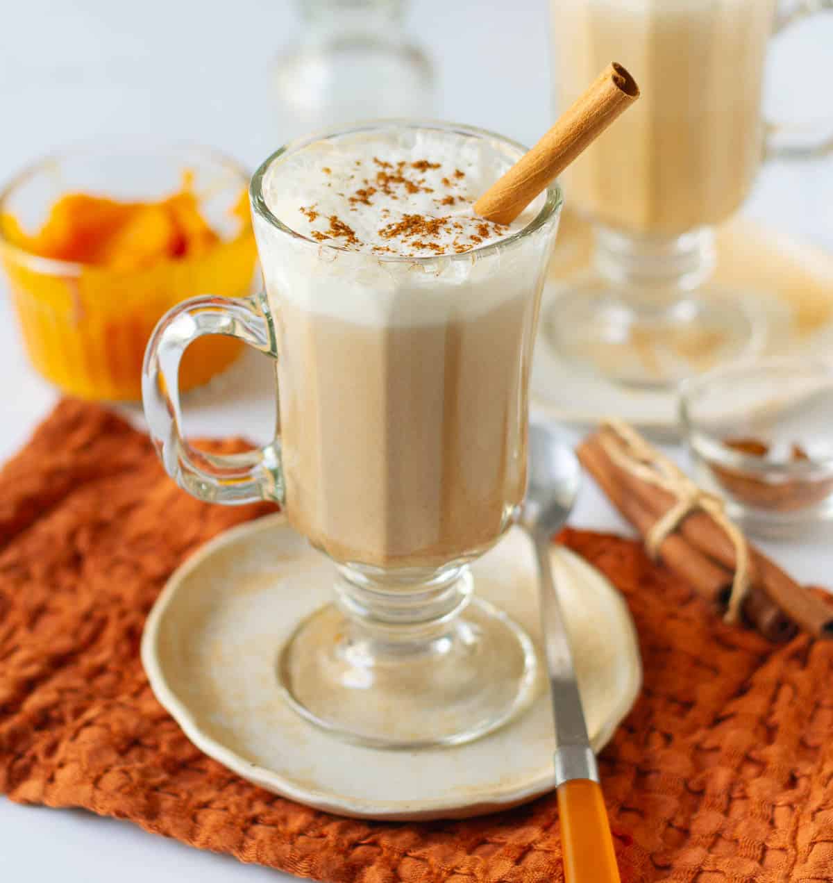 Latte in a glass mug topped with whipped cream, cinnamon and spices.