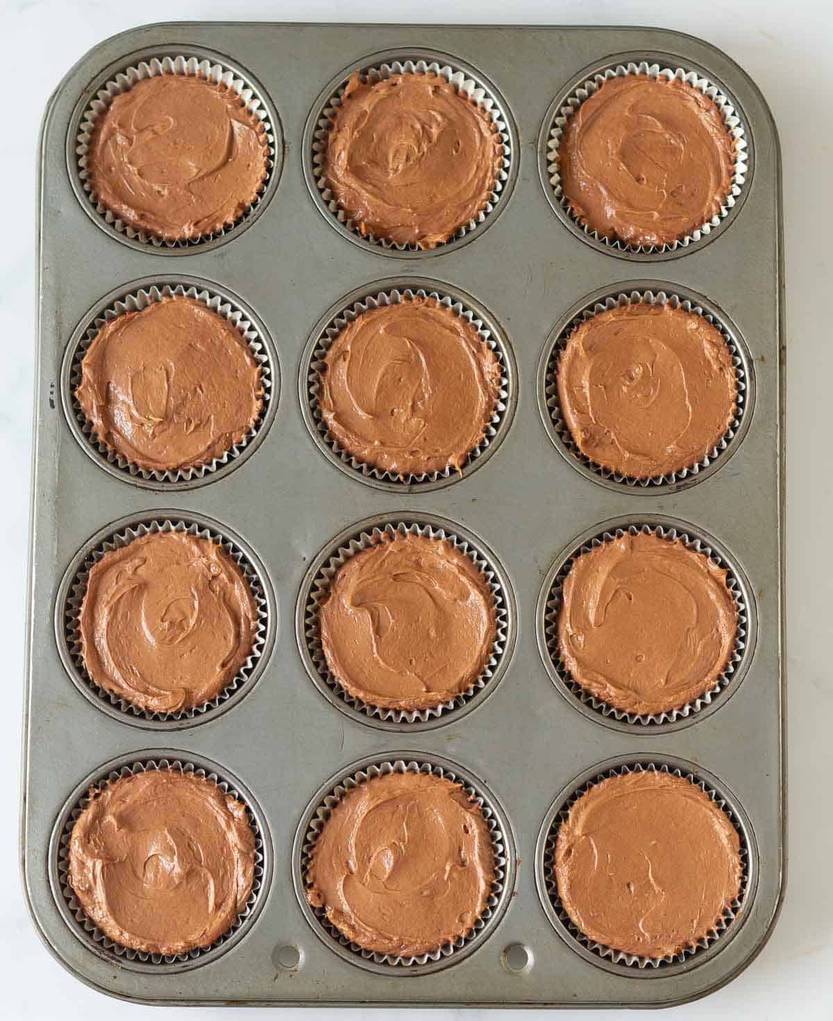 Chocolate cheesecake mixture in a muffin tray.