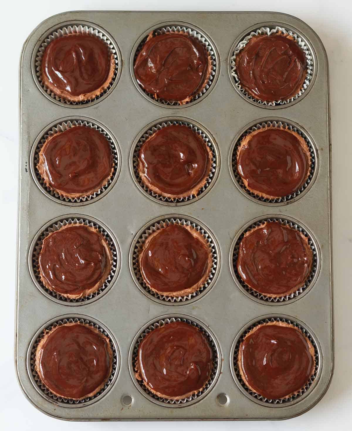 Chocolate cheesecakes topped with chocolate ganache in a muffin tray.