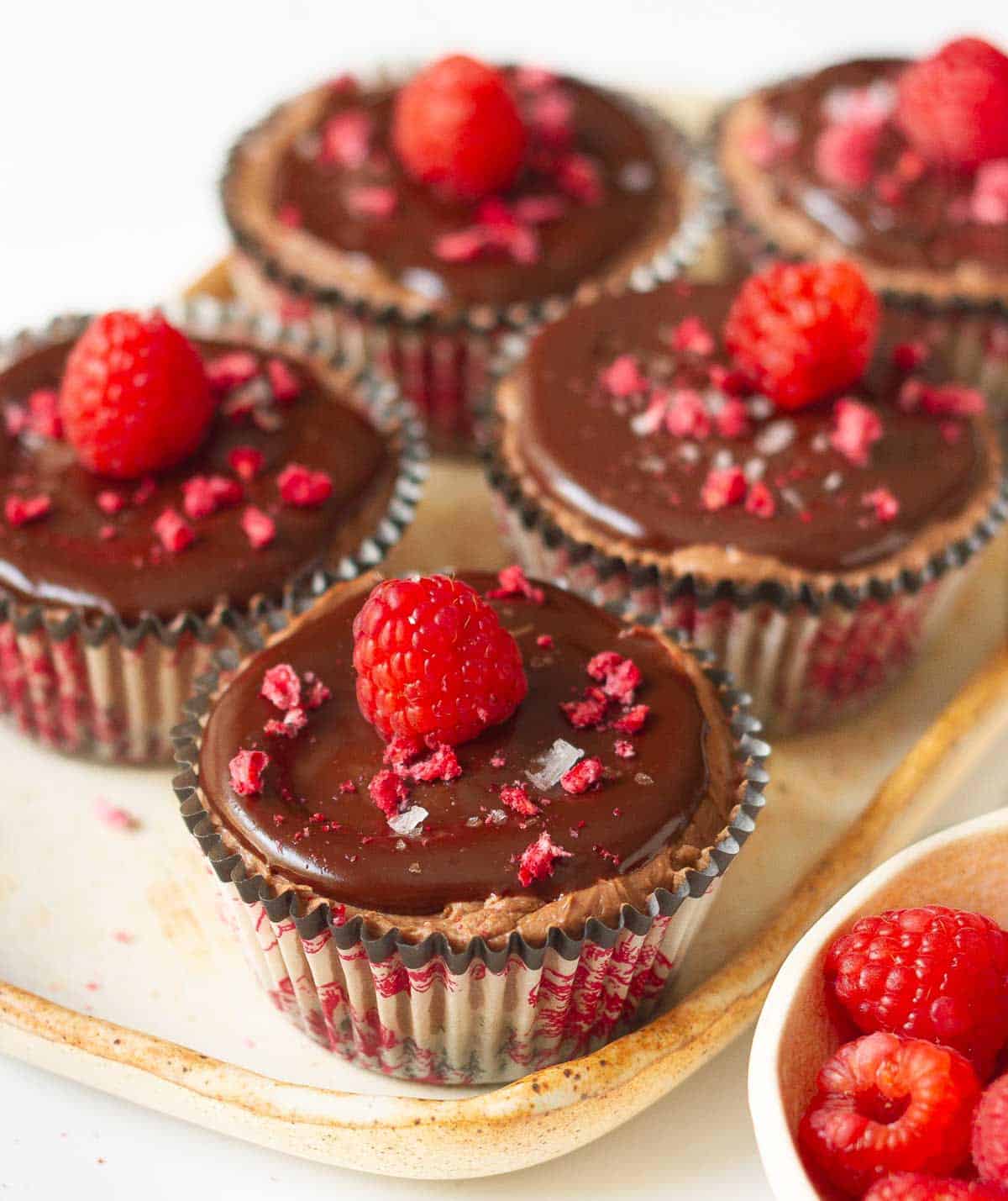 Mini chocolate cheesecakes topped with raspberries on a tray.