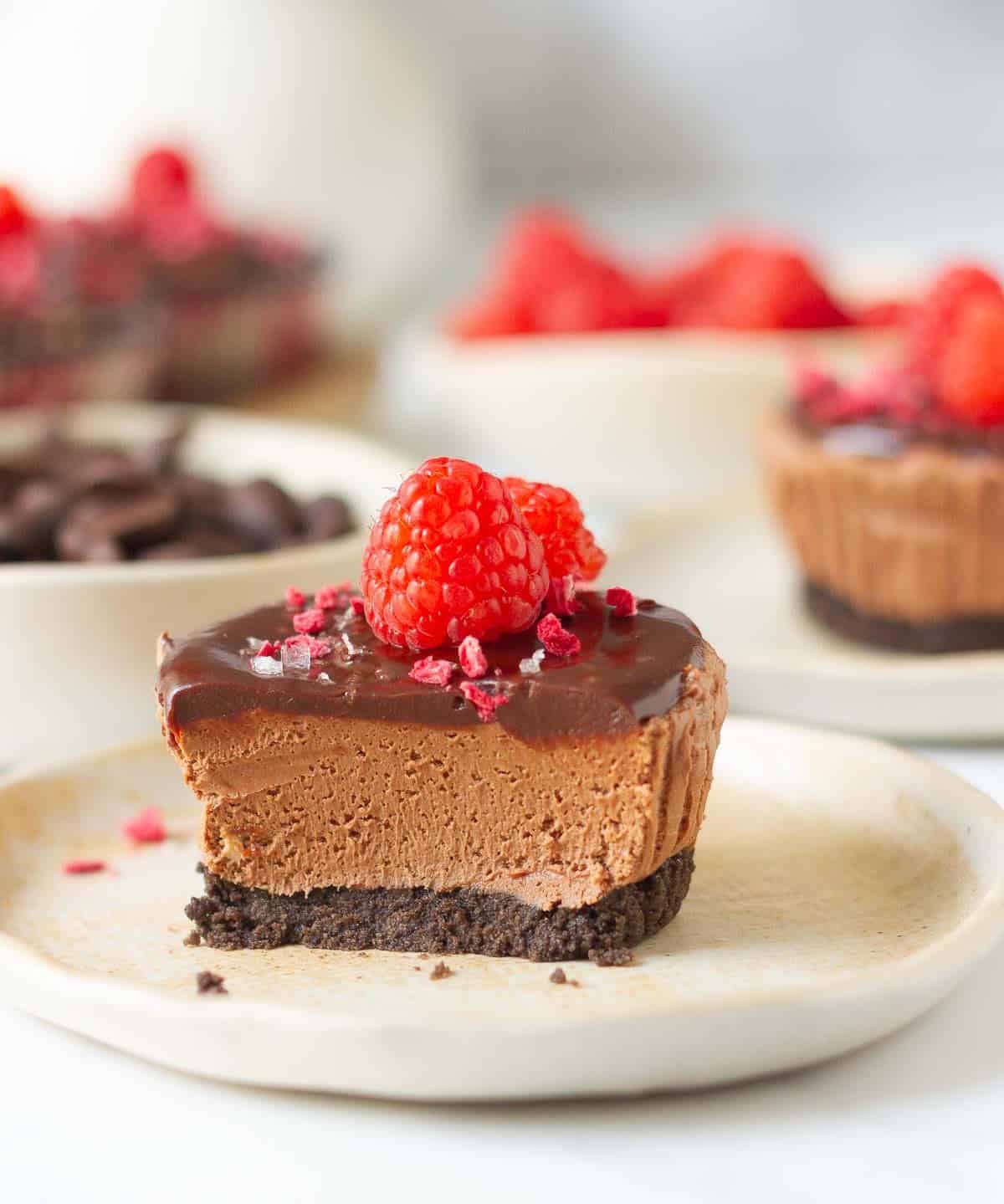 Half a chocolate cheesecake with raspberries on top on a plate.