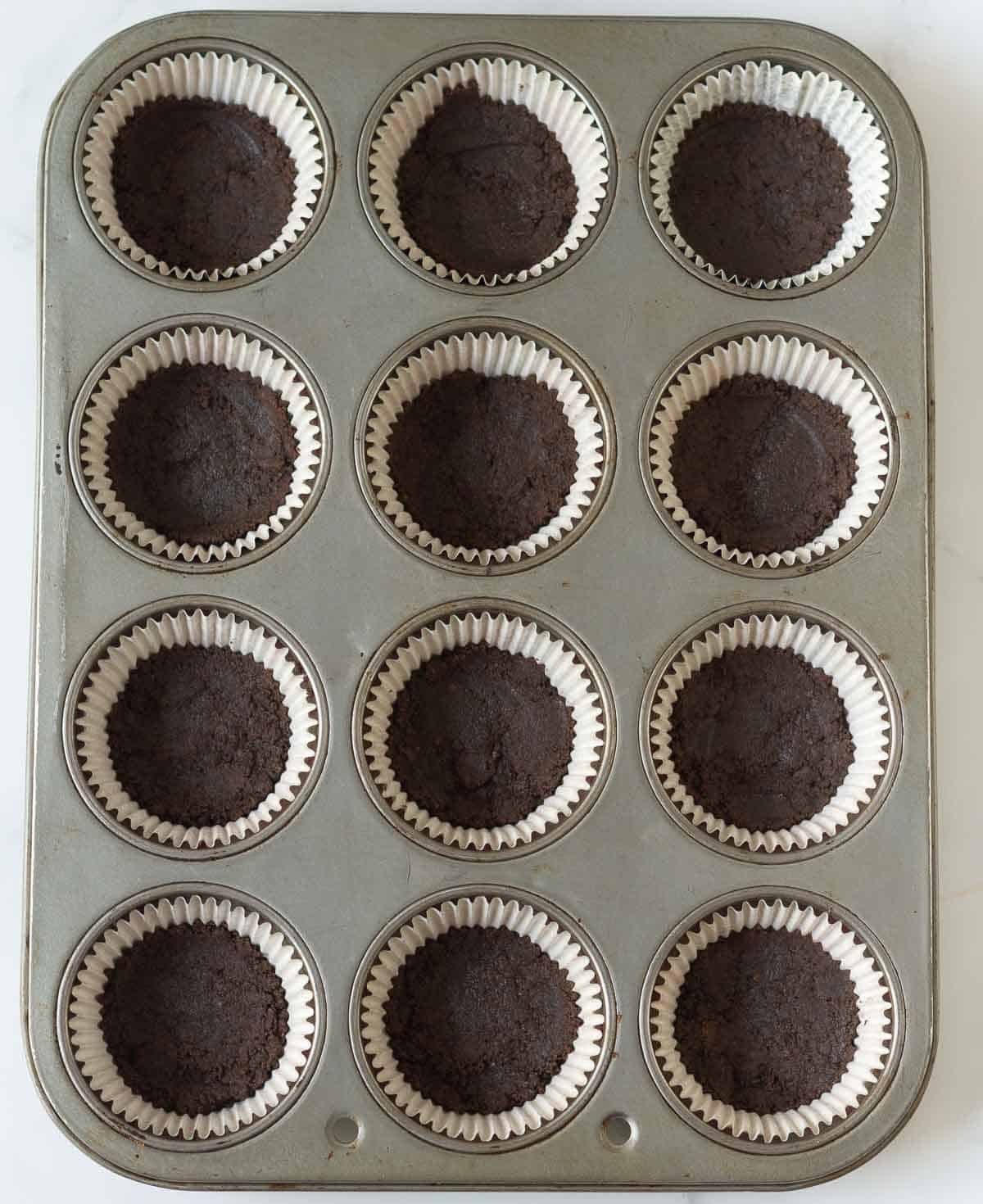 Cookie mixture in muffin tray lined with paper liners.
