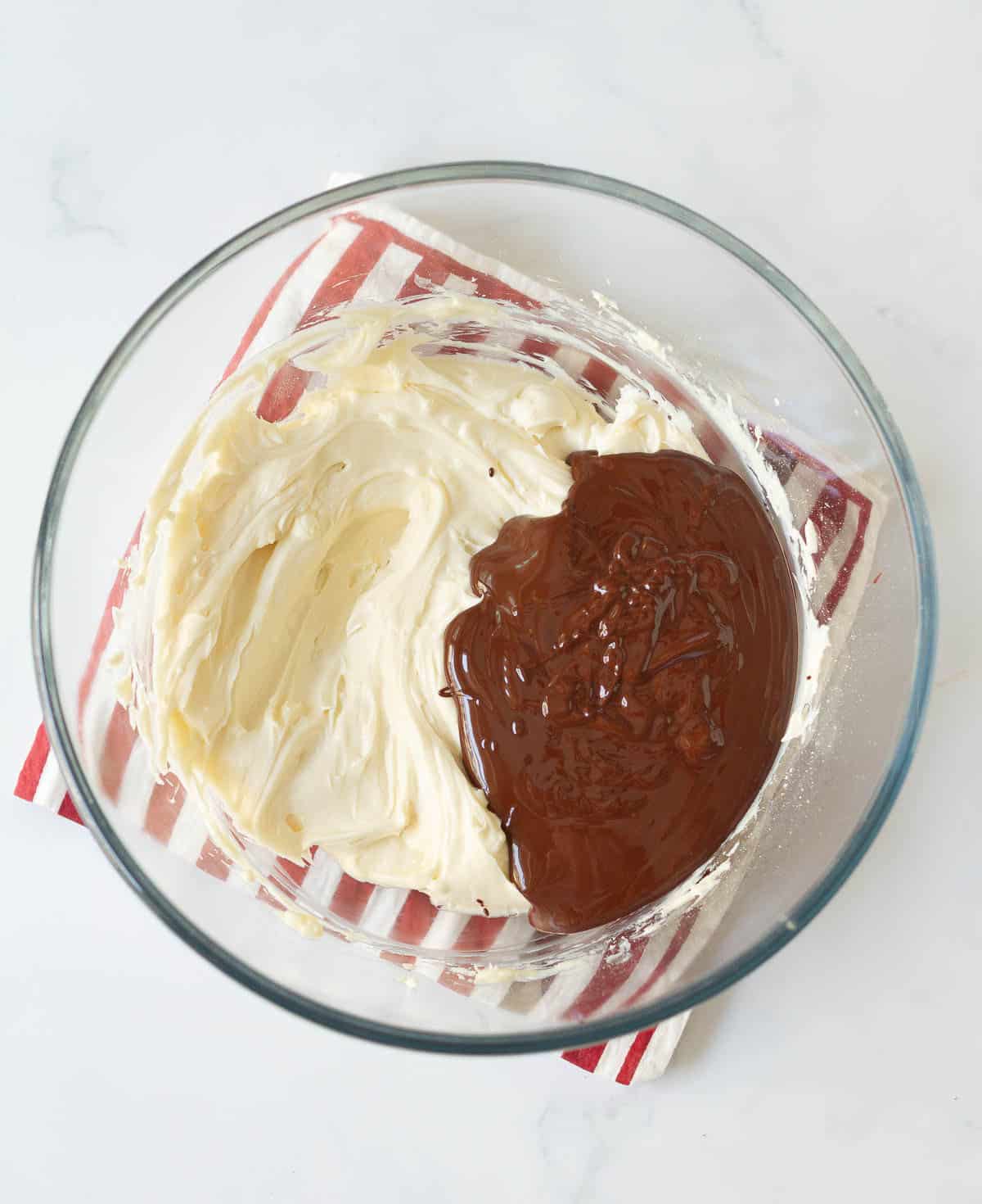 Melted chocolate on top of cream cheese mixture in a mixing bowl.