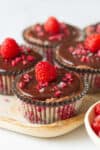 A tray with chocolate cheesecakes topped with raspberries.