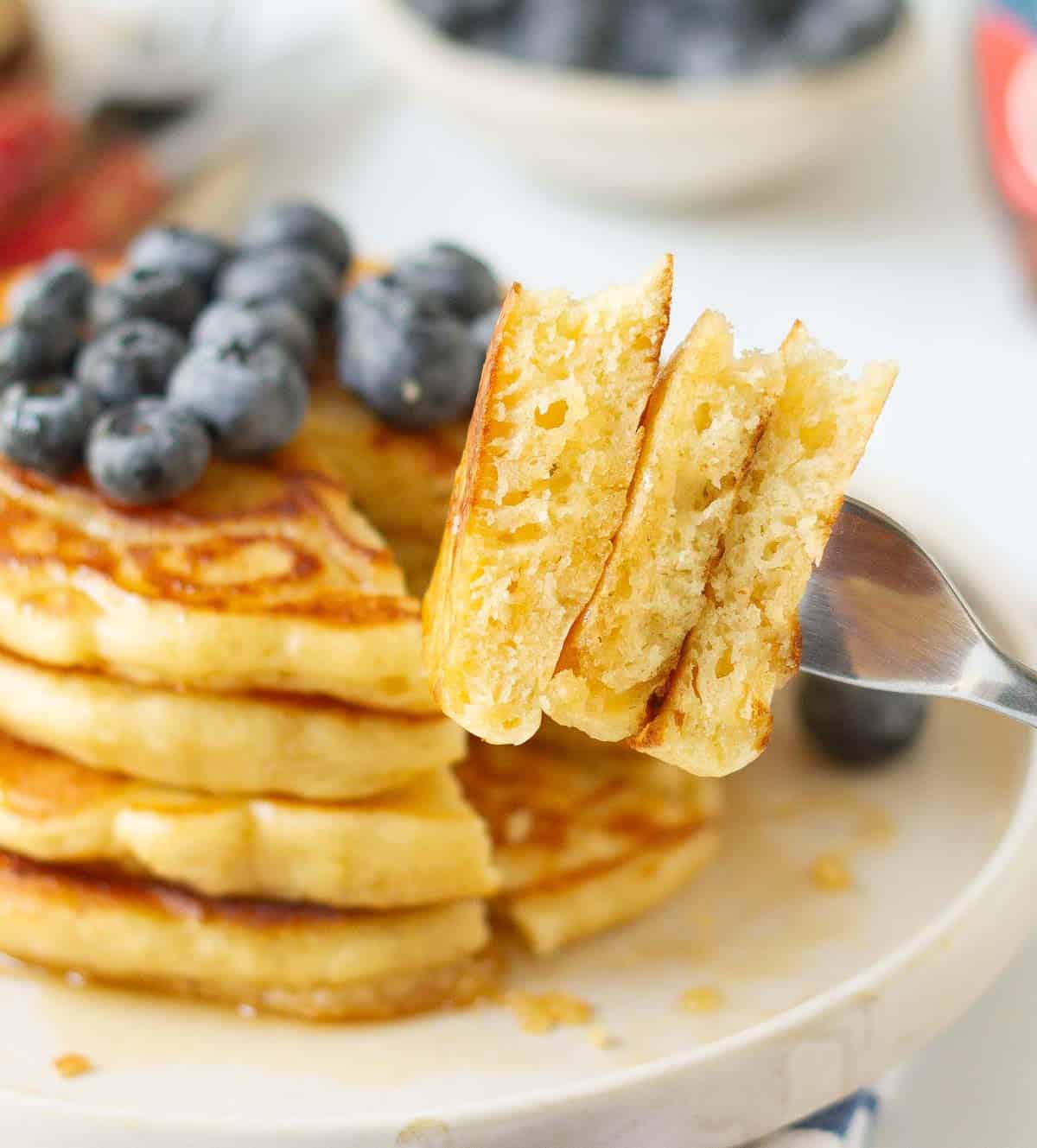 A fork with 3 small pieces of pancake from a stack topped with blueberries.